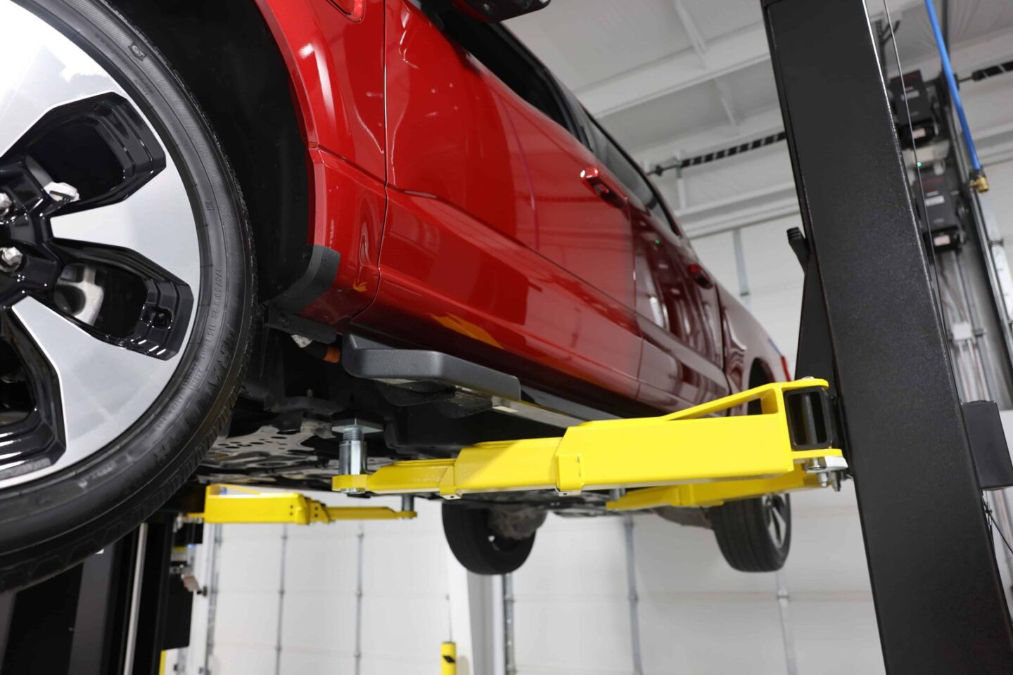 Red vehicle raised on a 2-post automotive lift with yellow swing arms in a clean professional shop