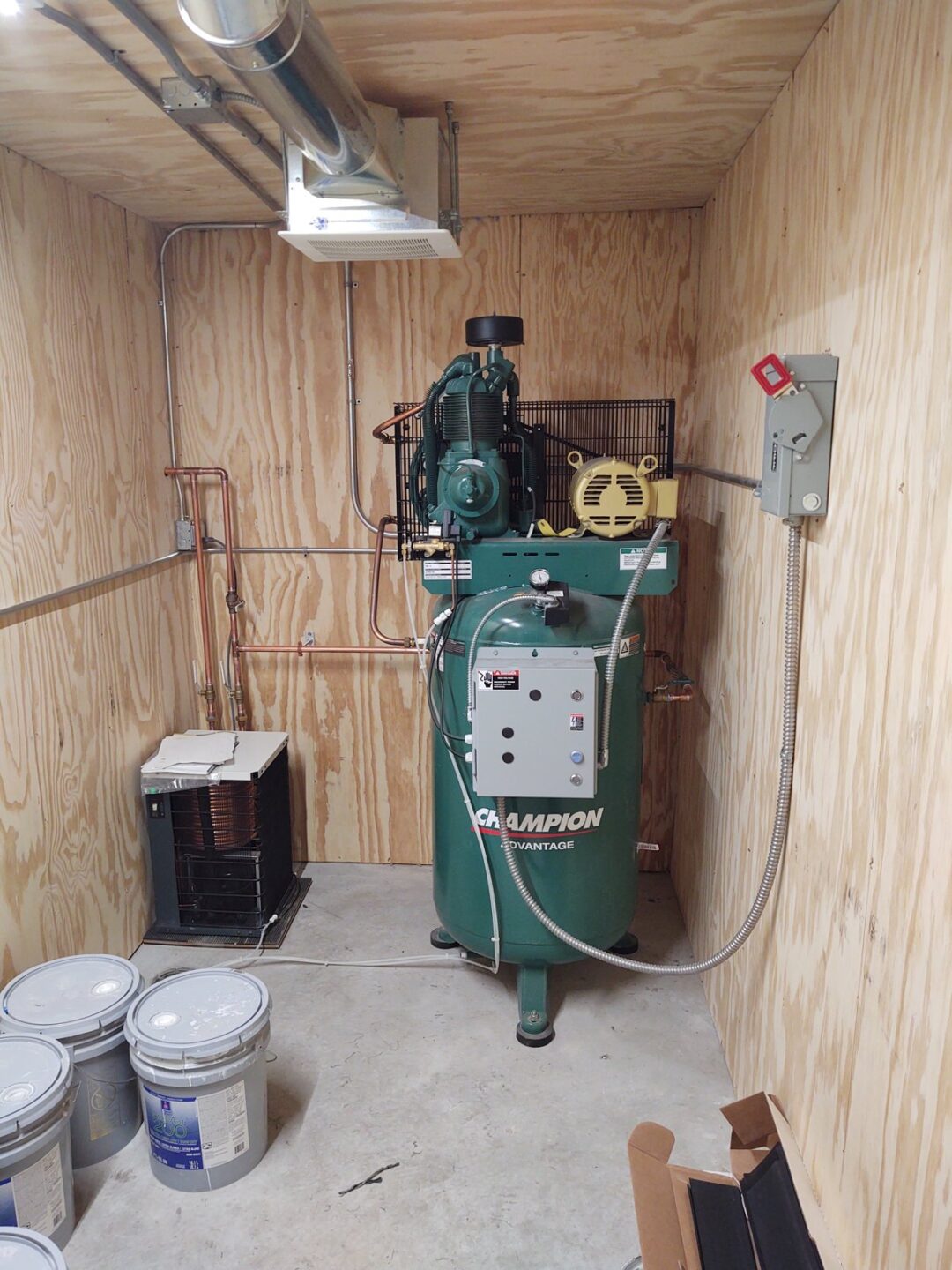 Champion Advantage air compressor with copper plumbing installed in plywood utility room for auto lift shop