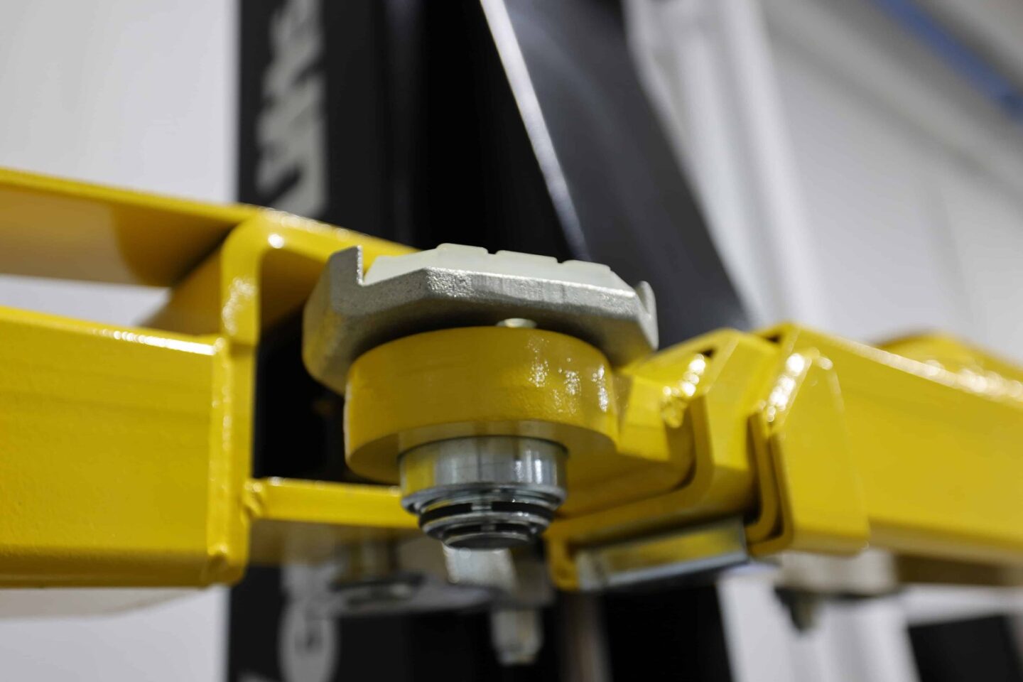 Close-up of yellow 2-post automotive lift swing arm pivot joint with rubber pad adapter