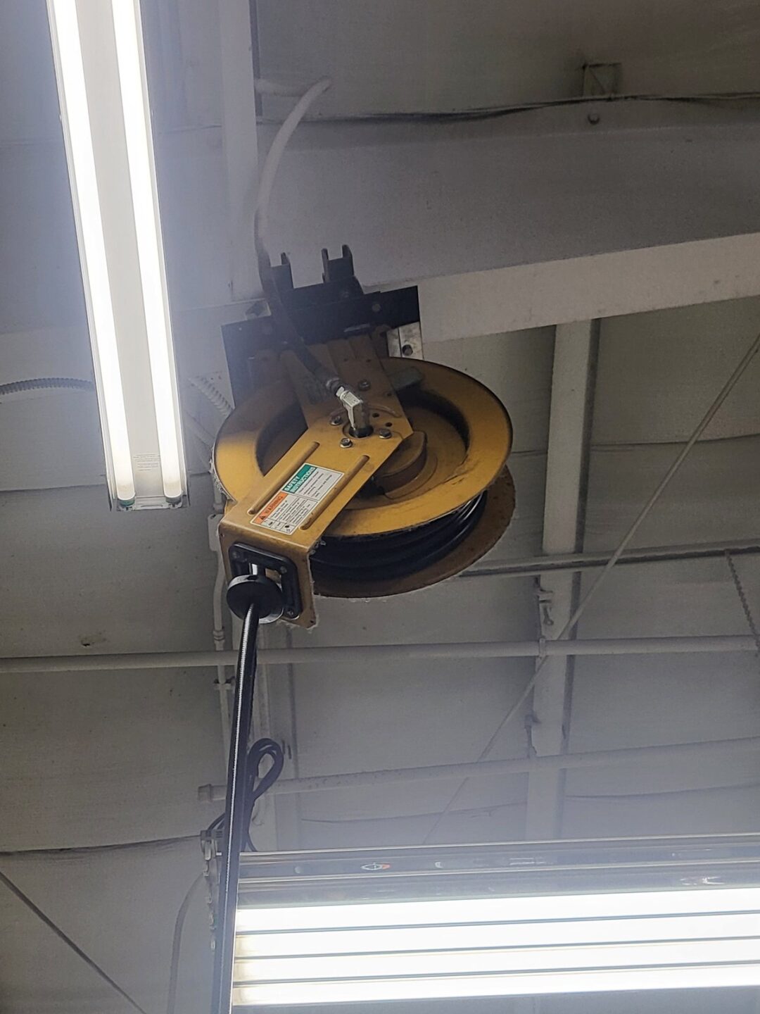 Yellow retractable hose reel mounted to ceiling in automotive service garage bay