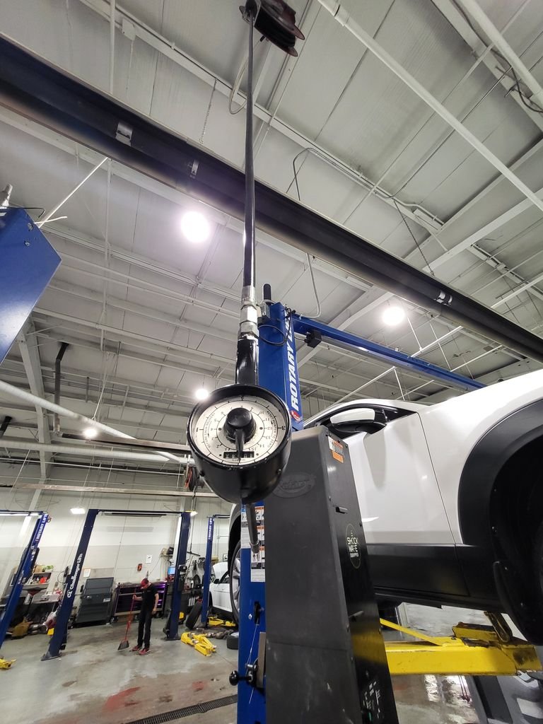 Rotary 2-post lift in busy auto shop with wheel alignment gauge in foreground