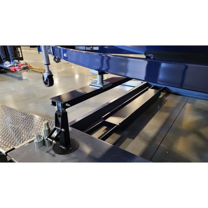 Close-up of automotive scissor lift base mechanism with adjustable runway and anchor hardware on shop floor