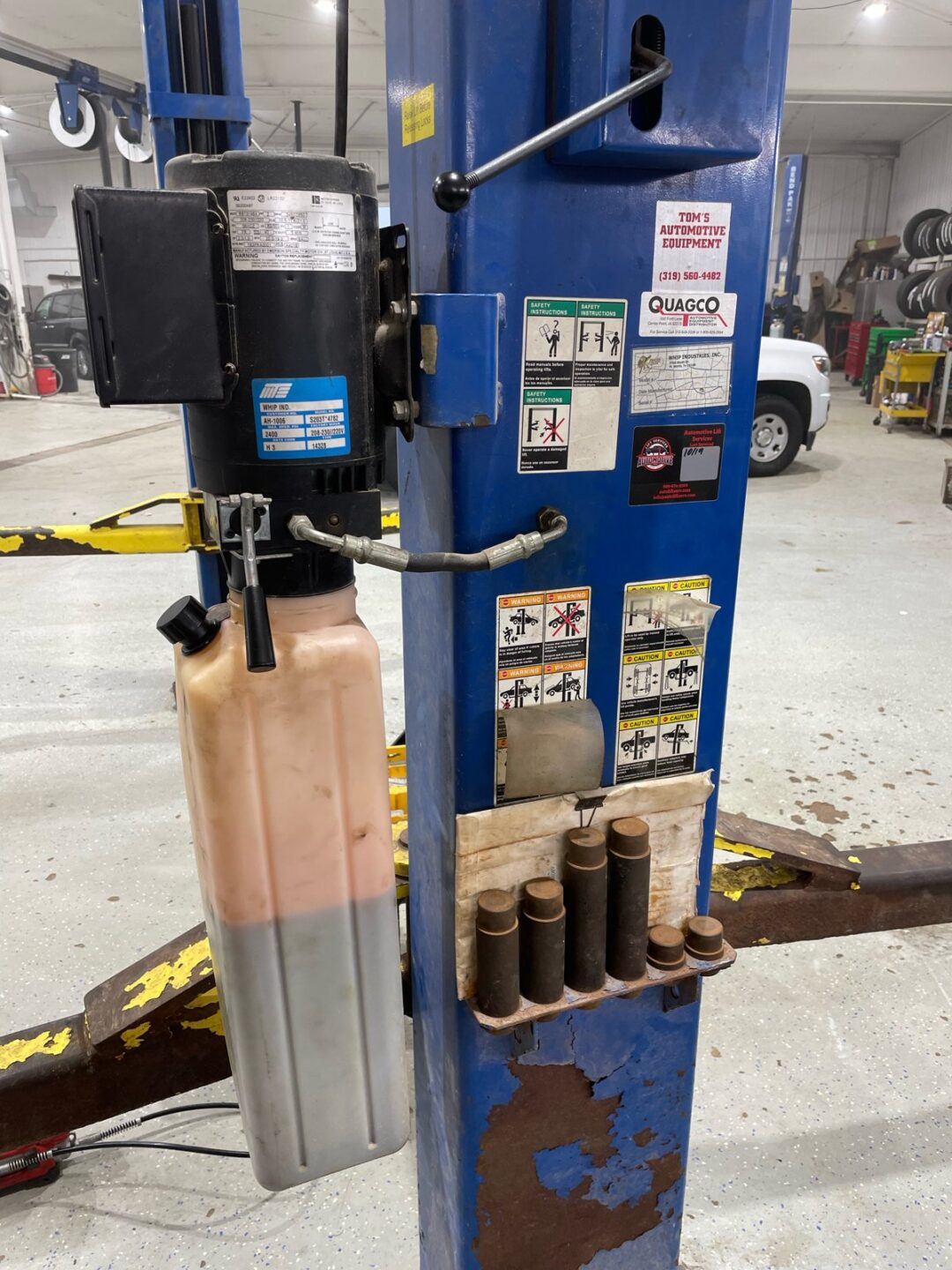 Worn automotive lift hydraulic power unit with degraded paint and contaminated fluid reservoir in Iowa shop