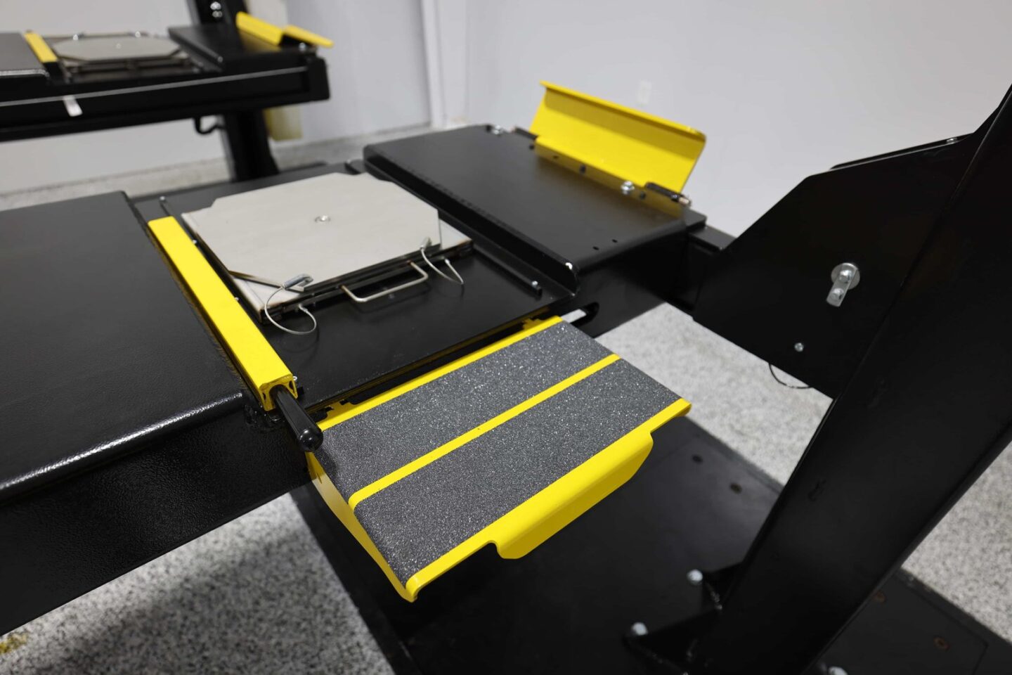 Close-up of 4-post automotive lift runway with yellow wheel risers, turn plates, and anti-slip drive-up ramp