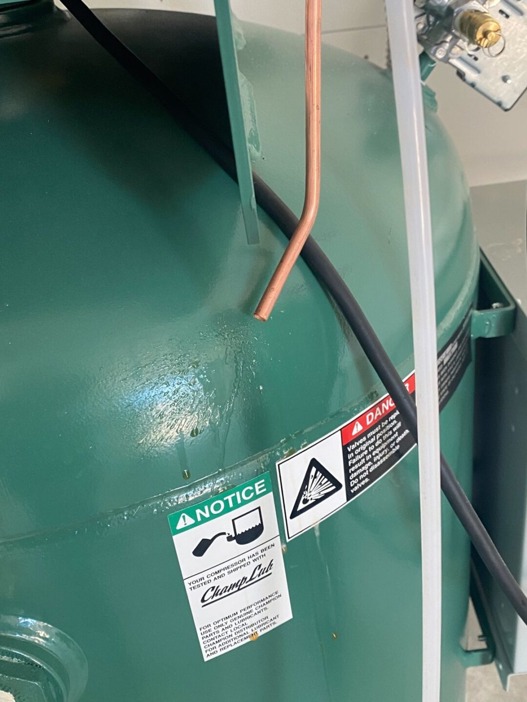 Closeup of green air compressor tank with copper line, safety notice and danger labels during shop install