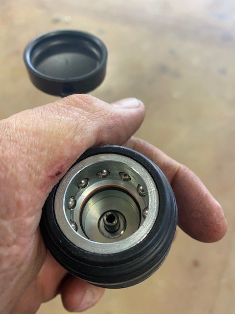 Technician holds hydraulic cylinder end cap with ball bearings removed during automotive lift repair service